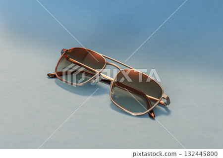 Sunglasses with silver frame and warm tinted lenses rest on blue surface in retro magazine style 132445800