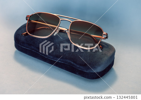 Modern sunglasses with metallic frame and tinted lenses rest on navy velvet case pastel backdrop 132445801