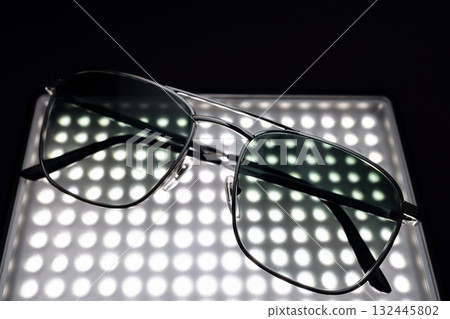 Contemporary fashion sunglasses with silver frame and tinted glass on glowing grid in dark scene Contemporary fashion sunglasses with silver frame and tinted glass on glowing grid in dark scene 132445802