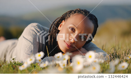 Woman relaxing in a meadow filled with flowers on a sunny day while enjoying nature and tranquility. The concept of mental health and unity with nature. 132446424
