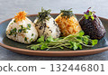 Colorful platter of onigiri featuring various fillings and toppings served with fresh microgreens 132446801