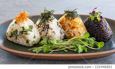 Colorful platter of onigiri featuring various fillings and toppings served with fresh microgreens 132446801