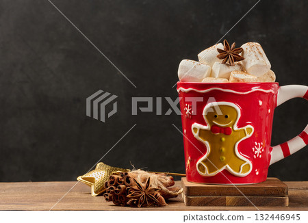 Hot chocolate in a red Christmas mug with a gingerbread man, marshmallows, star anise, and cinnamon on a wooden background Hot chocolate in a red Christmas mug with a gingerbread man, marshmallows, star anise, and cinnamon on a wooden background 132446945