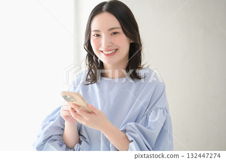 Japanese woman holding a smartphone and looking at the camera Japanese woman holding a smartphone and looking at the camera 132447274