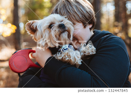 Adorable yorkshire terrier dog being held by a happy pet owner in the autumnal forest. A cute doggy on the hands of a woman. Real emotions of love. Adorable yorkshire terrier dog being held by a happy pet owner in the autumnal forest. A cute doggy on the hands of a woman. Real emotions of love. 132447845