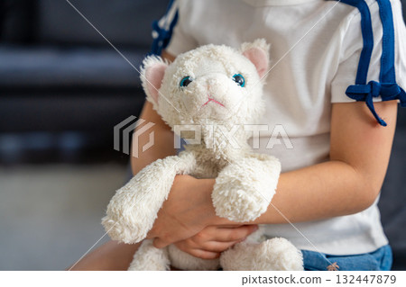 Child holding a well-worn plush toy tightly in both hands. Emotional connection to a beloved object that provides comfort, security, and a sense of familiarity in early childhood. Child holding a well-worn plush toy tightly in both hands. Emotional connection to a beloved object that provides comfort, security, and a sense of familiarity in early childhood. 132447879