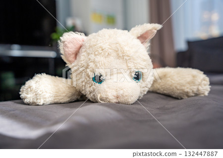 Worn white plush cat toy lying on a couch. Beloved childhood item that brings emotional comfort, personal meaning, and a sense of security over the years. Worn white plush cat toy lying on a couch. Beloved childhood item that brings emotional comfort, personal meaning, and a sense of security over the years. 132447887