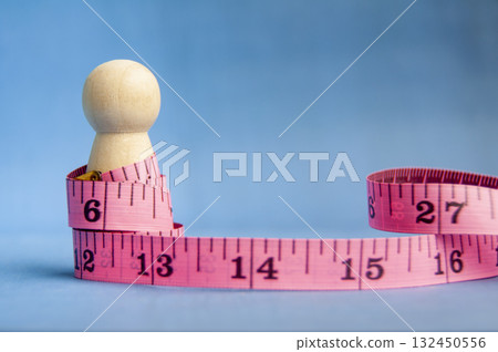 Wooden peg surrounded by pink measuring tape symbolizing health and balance with customizable space for text or ideas. 132450556