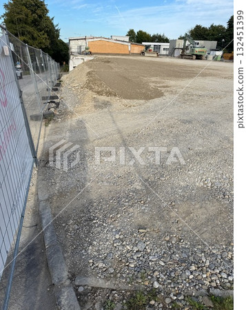 Fence is in front of a building with a lot of gravel 132451399