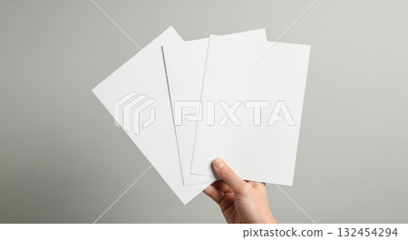 Hand holding blank sheets of paper on a neutral background for design mockup 132454294
