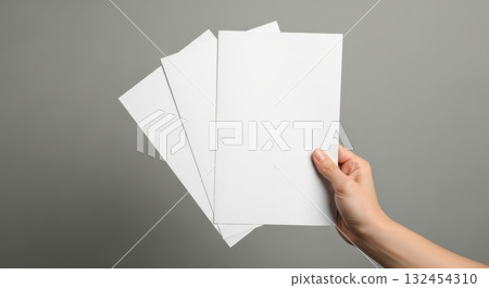 Hand holding three blank white flyers against a gray background Hand holding three blank white flyers against a gray background 132454310