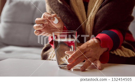 Senior woman holding tablet above glass of water wearing warm sweater 132454505