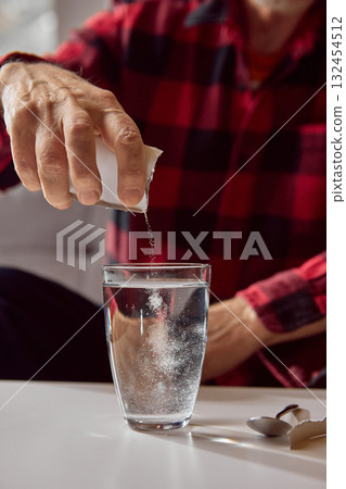 Senior man pouring granular supplement powder into transparent glass with water Senior man pouring granular supplement powder into transparent glass with water 132454512