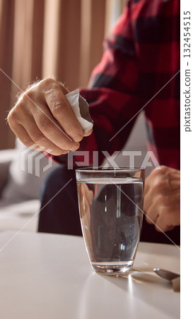 Hand pouring white medicine powder from sachet into glass of water 132454515