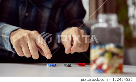 Senior hands choosing colorful pills on white table near medicine bottle Senior hands choosing colorful pills on white table near medicine bottle 132454525