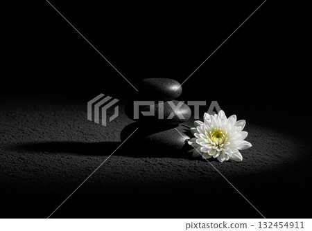 Zen balance, smooth dark stones and a delicate white flower in focused light 132454911