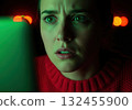 Frightened woman face illuminated by intense green light, expressing confusion 132455900