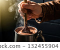 Hand stirring steaming hot chocolate in a vintage pewter tankard with a wooden spoon 132455904