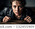 Fierce woman in leather jacket, leaning forward with a powerful, intense gaze. 132455909