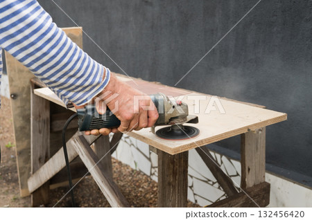 Caucasian male adult sanding wood with power tool on outdoor workbench 132456420