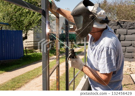 Mature caucasian male welding metal frame outdoors. National Welding Month Mature caucasian male welding metal frame outdoors. National Welding Month 132456429