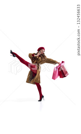 Confident woman in brown coat talking on phone while holding shopping bags 132456633