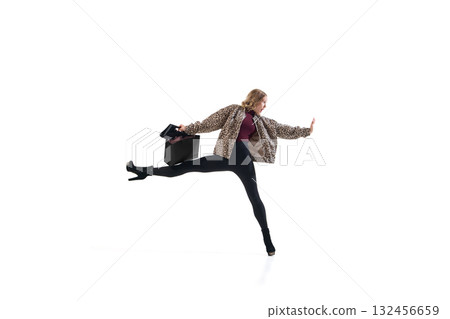 Fashion model in leopard jacket stretching leg while holding shopping bag in expressive pose Fashion model in leopard jacket stretching leg while holding shopping bag in expressive pose 132456659