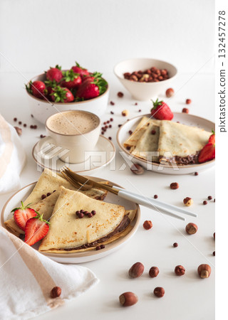 Crepes with chocolate hazelnut spread, strawberries and hazelnuts on a white wooden table. Crepes with chocolate hazelnut spread, strawberries and hazelnuts on a white wooden table. 132457278