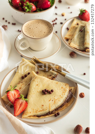 Crepes with chocolate hazelnut spread, strawberries and hazelnuts on a white wooden table. Crepes with chocolate hazelnut spread, strawberries and hazelnuts on a white wooden table. 132457279