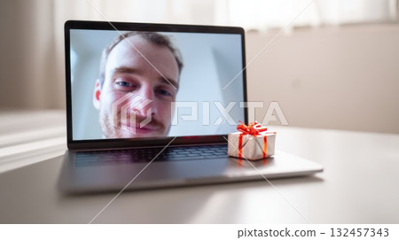 Smiling Man On Laptop Video Call With Gift Box On Keyboard In Home Office Smiling Man On Laptop Video Call With Gift Box On Keyboard In Home Office 132457343