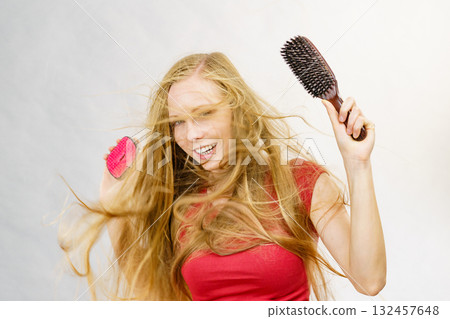 Blonde girl long blowing hair holds two brushes 132457648
