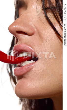 Close-up side view woman biting chili pepper with glowing lips and clean skin 132457697