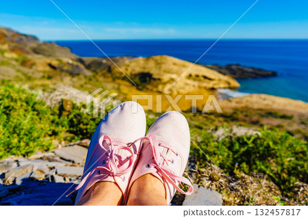Female legs in sneakers against coast landscape, Spain. Female legs in sneakers against coast landscape, Spain. 132457817