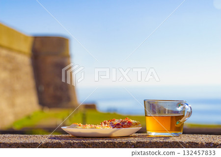 Tea mug and pizza slices on plate, outdoors 132457833