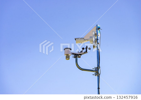 Security video camera and wind indicator against sky. Security video camera and wind indicator against sky. 132457916