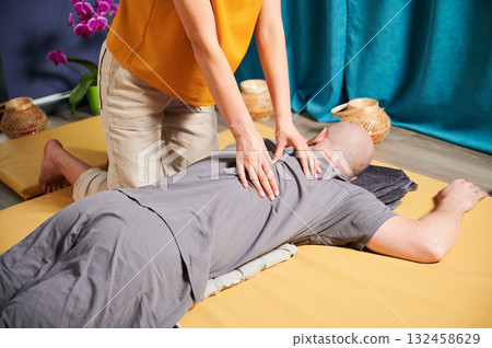 Masseuse making thai yoga massage. Cropped view of woman therapist doing traditional massage treatment for male patient indoors. Bald client meditating, enjoying hand massage in calm atmosphere. 132458629