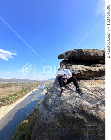 Man Sitting on Cliff Overlooking River and Valley Man Sitting on Cliff Overlooking River and Valley 132459000