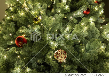 Close-up of decorated Christmas tree branches with glowing lights and elegant ornaments in red and gold tones Close-up of decorated Christmas tree branches with glowing lights and elegant ornaments in red and gold tones 132459228