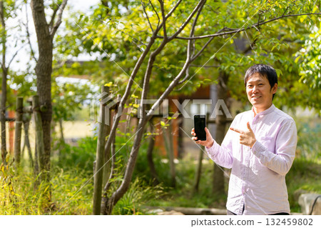 一位微笑的男士指著他的智慧型手機螢幕進行介紹,這是一張行動應用程式介紹的圖片 一位微笑的男士指著他的智慧型手機螢幕進行介紹,這是一張行動應用程式介紹的圖片 132459802