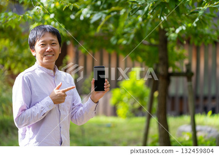 一位微笑的男士指著他的智慧型手機螢幕進行介紹,這是一張行動應用程式介紹的圖片 一位微笑的男士指著他的智慧型手機螢幕進行介紹,這是一張行動應用程式介紹的圖片 132459804