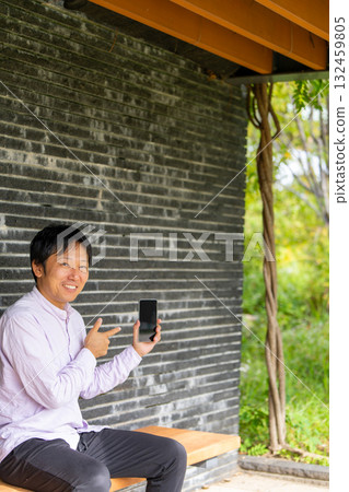 A smiling man pointing at the screen of his smartphone and introducing it, an image of a mobile app introduction 132459805