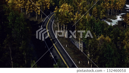 Curving gently, the road invites travelers into a serene landscape where golden and green trees create a stunning autumn tableau. Natures beauty envelops the path inviting exploration. 132460058