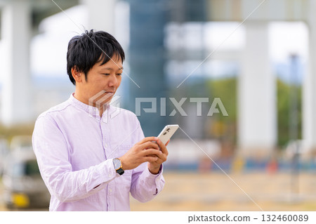 A business man operating a smartphone and checking notifications outdoors 132460089
