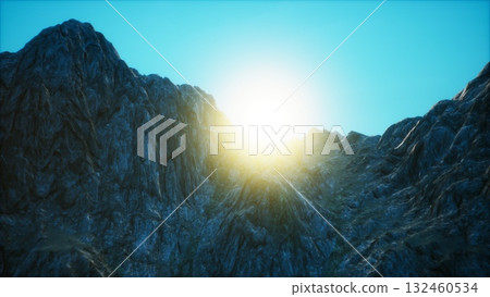 Golden rays spill over rugged mountain tops, painting the rocky landscape in light. The tranquil moment captures the beauty of dawn in a remote, untouched wilderness. 132460534