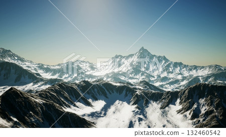 Breathtaking snow covered peaks rise dramatically against a vivid blue sky, illuminated by the warm glow of the sun setting over the mountainous landscape. 132460542