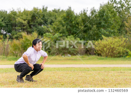 A man stretching in the square, bending his knees on the grass to loosen up his body 132460569