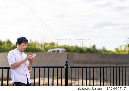 A man operating a smartphone with the sea in the background | Plenty of copy space A man operating a smartphone with the sea in the background | Plenty of copy space 132460747