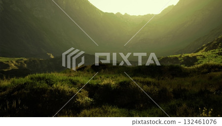 Soft sunlight bathes the lush hills and valleys in a serene location, creating a tranquil atmosphere at golden hour. The vibrant greenery enhances the scenic beauty of the area. 132461076