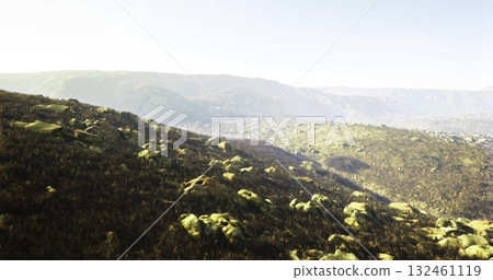 Rolling hills covered in green vegetation and rocky formations stretch across the landscape under a bright sky. The scene captures the tranquility of nature in a serene environment. Rolling hills covered in green vegetation and rocky formations stretch across the landscape under a bright sky. The scene captures the tranquility of nature in a serene environment. 132461119