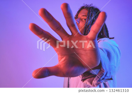 Young man with dreadlocks listening music on headphones and gesturing stop with hand in neon light Young man with dreadlocks listening music on headphones and gesturing stop with hand in neon light 132461310